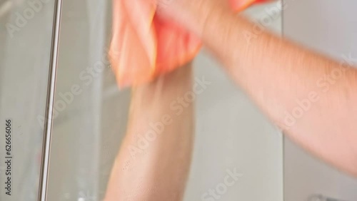 Cleaning service concept. Cropped view of man wiping mirror with rag, standing in bathroom. Householder make daily routine work at home