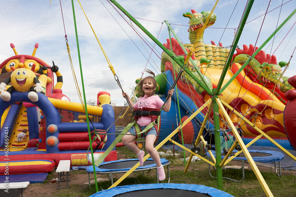 Summer attraction for active children. Happy girl bouncing on elastic bands on the trampoline.