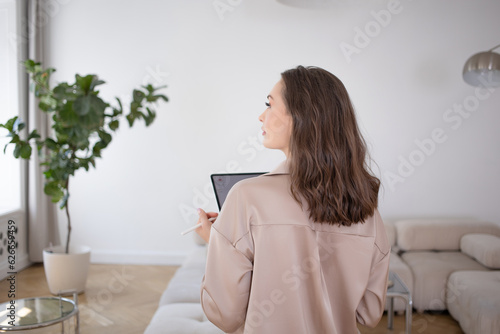 A business woman in a loose beige suit holds a digital tablet in her hands, a photo in the interior, calm pastel colors