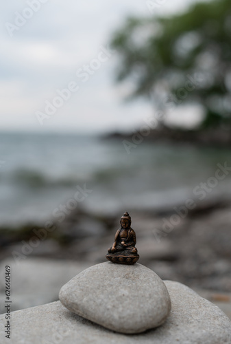 Close up of little bronze budda Budha Budda Gautama on gray rock outdoors near lake. Beautiful lake landscape near lake in Ontario, Toronto. Symbol of buddhism.