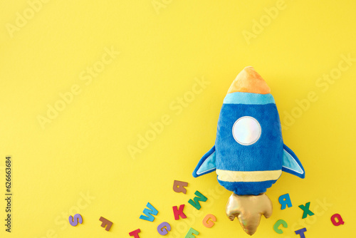 Back to school concept. Top view composition of rocket-shaped pencil case, colorful letters on yellow background with empty space for promo or message