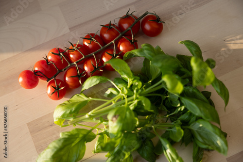 Fresh Italian sweet basil and tomatoes on a kitchen table in front of an open window at sunset