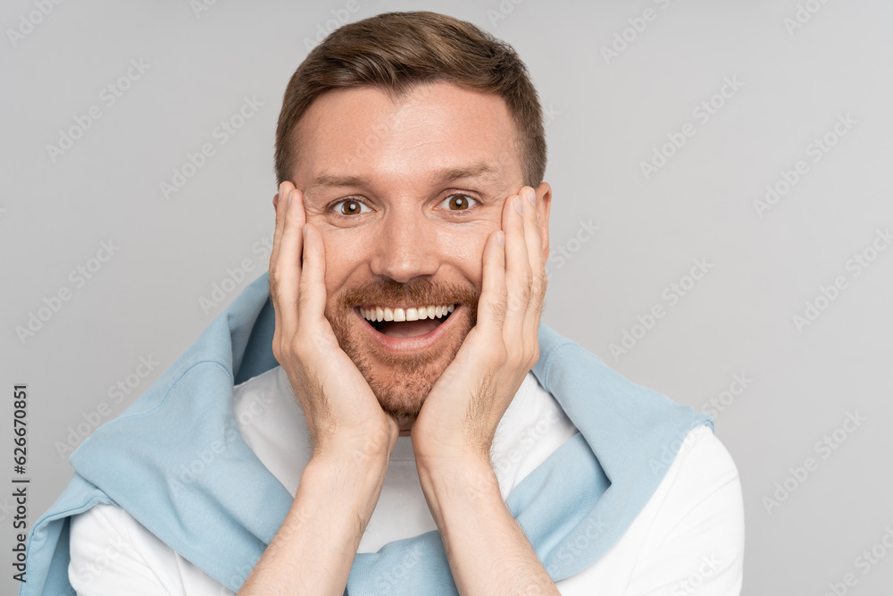 Smiling handsome man with mouth open, showing his white straight teeth, touching face with hands. Excited guy getting amazed of positive news, surprise, lottery win, success at work, isolated on gray. Smiling handsome man with mouth open, showing his white straight teeth, touching face with hands. Excited guy getting amazed of positive news, surprise, lottery win, success at work, isolated on gray.