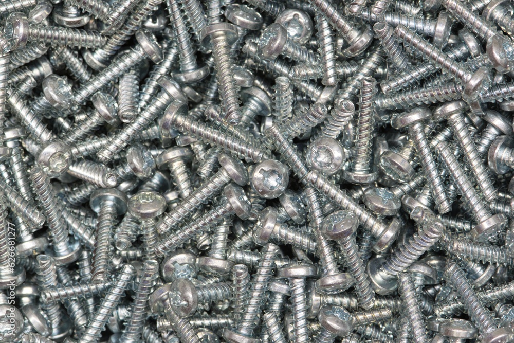Six-lobe metal Torx screws scattered loosely. Work tools and hardware accessories, directly above view. Six-lobe metal Torx screws scattered loosely. Work tools and hardware accessories, directly above view.