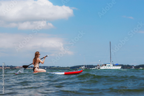 Young woman riding stand up paddle board in the sea. Healthy and fit life in the nature.