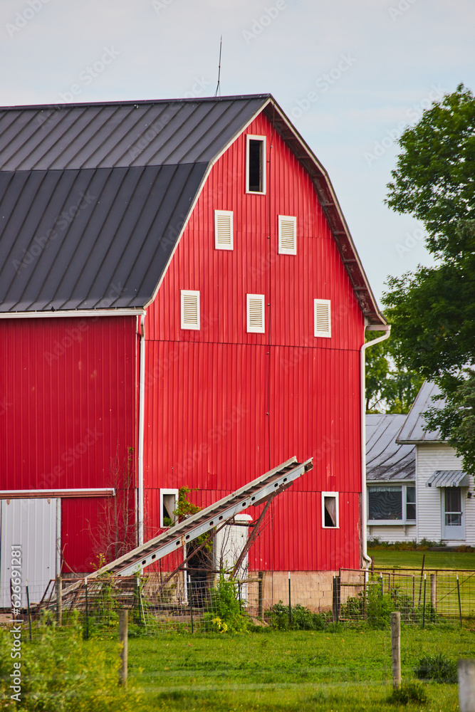Farm with giant red barn and tall ladder on other side of wire fence Farm with giant red barn and tall ladder on other side of wire fence