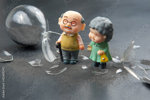 miniature people. couple of elderly people near a broken hourglass. life time crisis. the concept of the end of life for a person