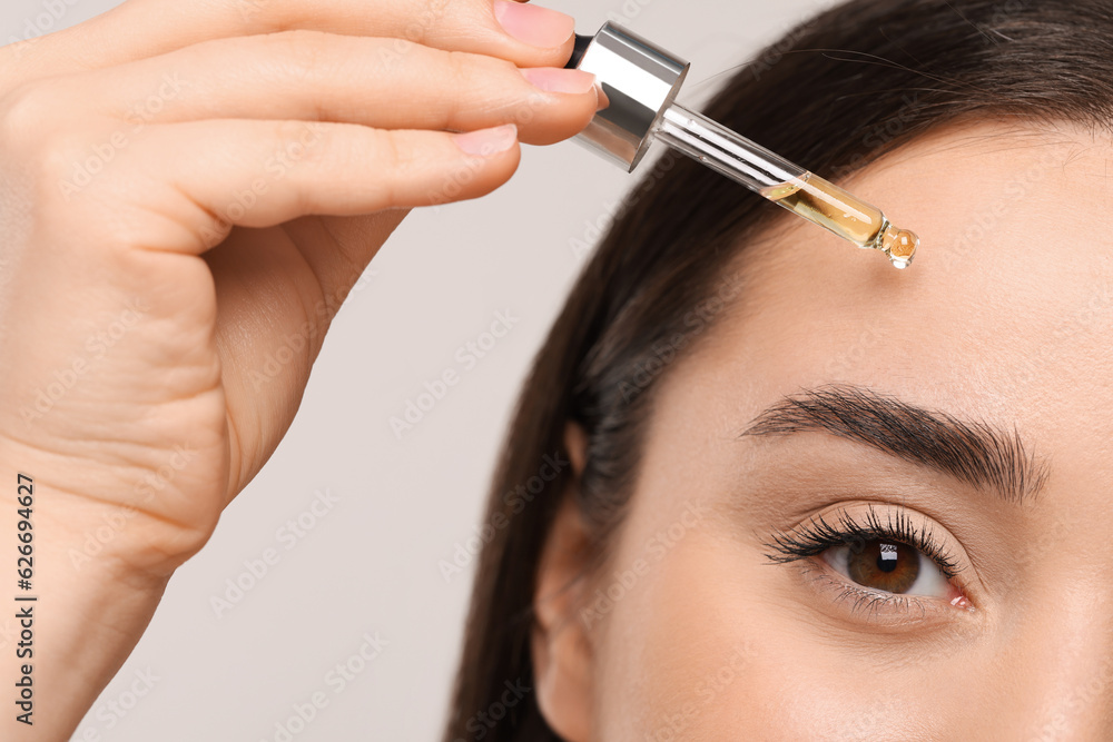 Young woman applying essential oil onto face on light grey background, closeup Young woman applying essential oil onto face on light grey background, closeup