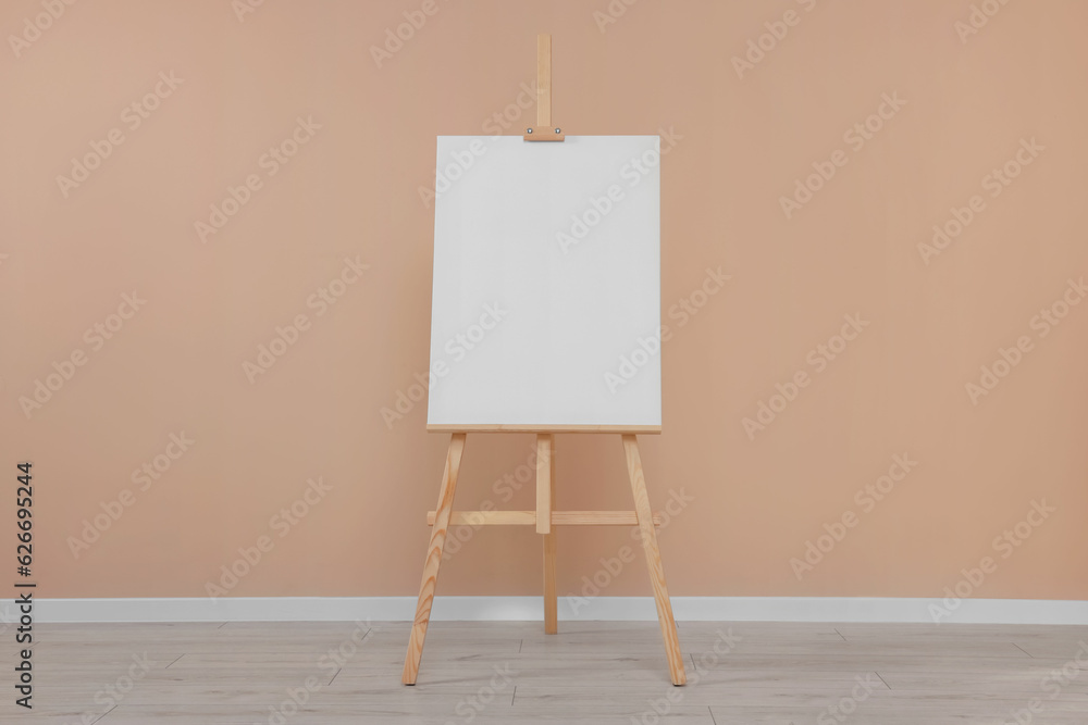 Wooden easel with blank canvas near beige wall indoors. Wooden easel with blank canvas near beige wall indoors.