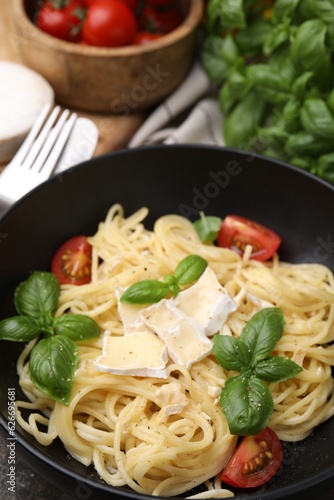 Delicious pasta with brie cheese, tomatoes and basil leaves in bowl, closeup