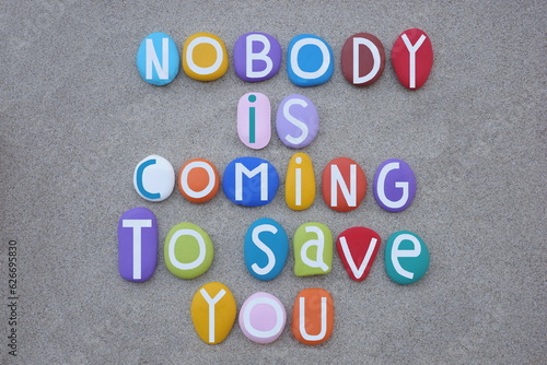 Nobody is coming to save you, creative slogan composed with multi colored stone letters over beach sand