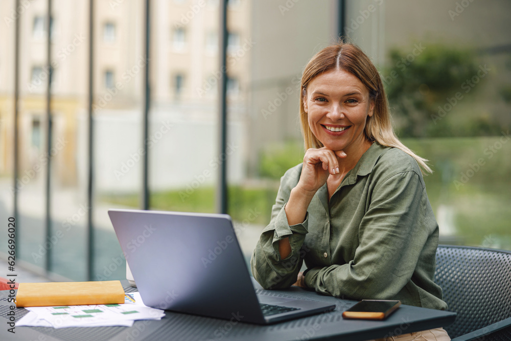 Smiling woman sales manager working on laptop in cafe terrace and looking at camera Smiling woman sales manager working on laptop in cafe terrace and looking at camera