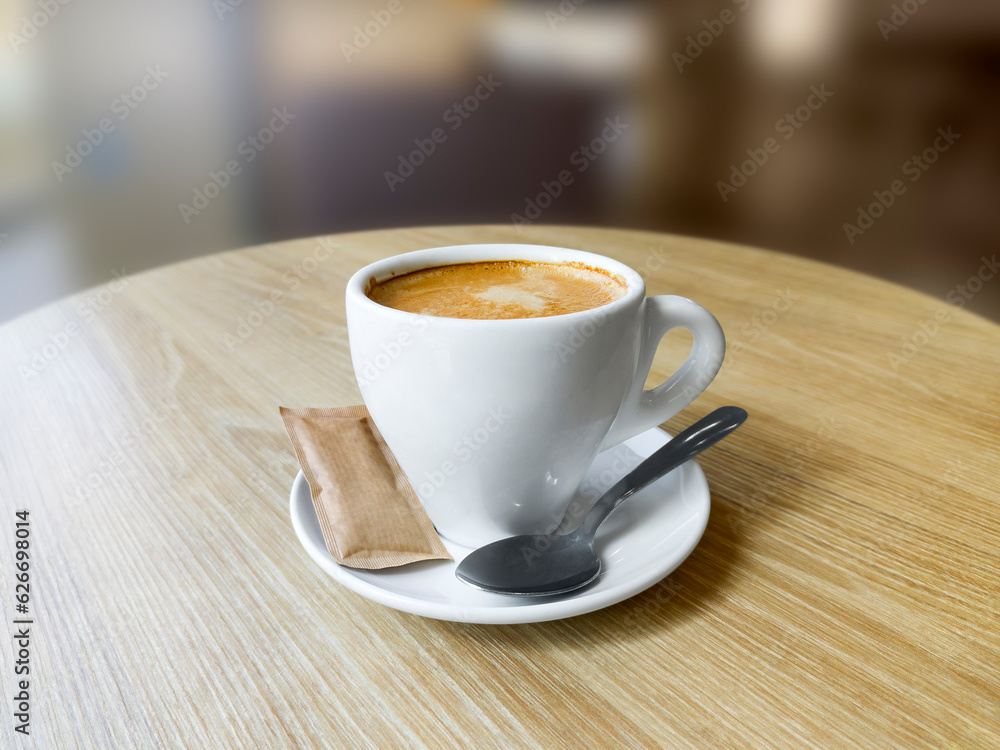 Coffee cup with saucer, teaspoon and a packet of brown sugar on a round wooden table Coffee cup with saucer, teaspoon and a packet of brown sugar on a round wooden table