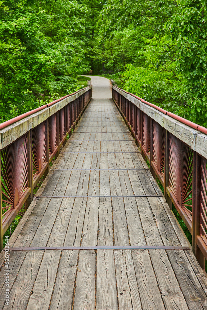 Boardwalk with rusty metal bar railing and worn wooden beams and planks leading to trail