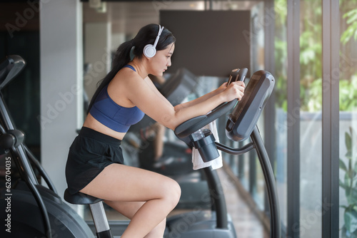 Concentrated young woman in sportswear listening to music in headphones. burning calories on spin bike at gym.