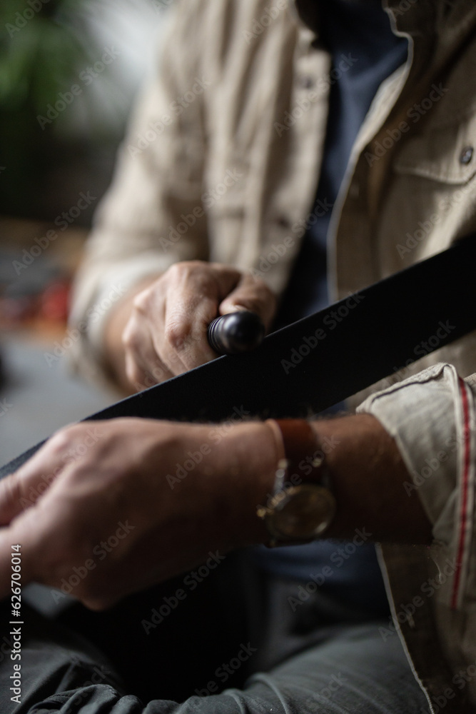 Man doing leatherwork, in a leather working workshop, making a black leather belt