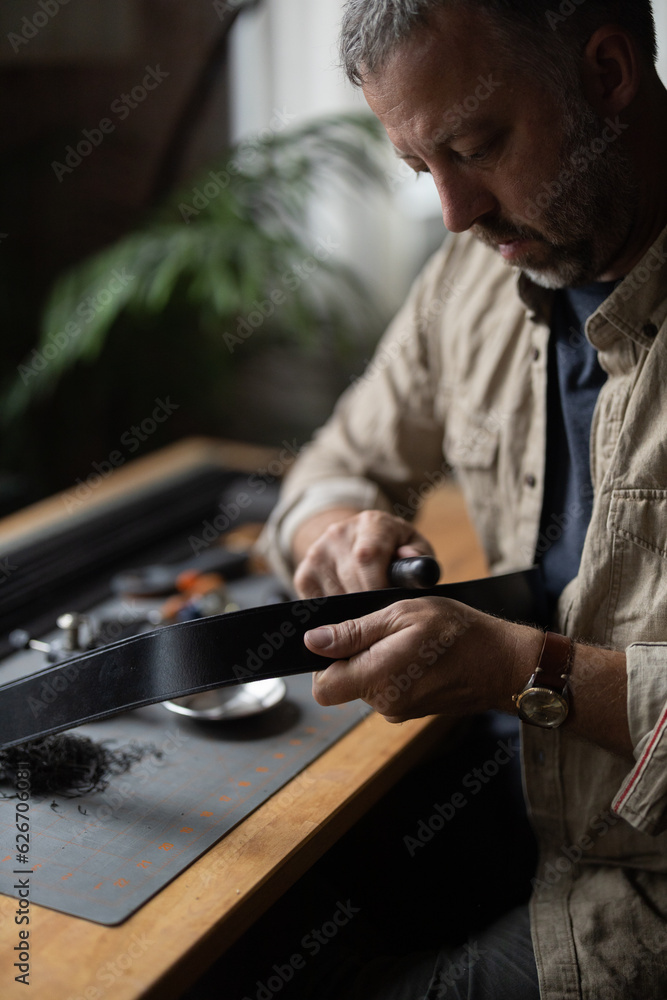 Man doing leatherwork, in a leather working workshop, making a black leather belt Man doing leatherwork, in a leather working workshop, making a black leather belt