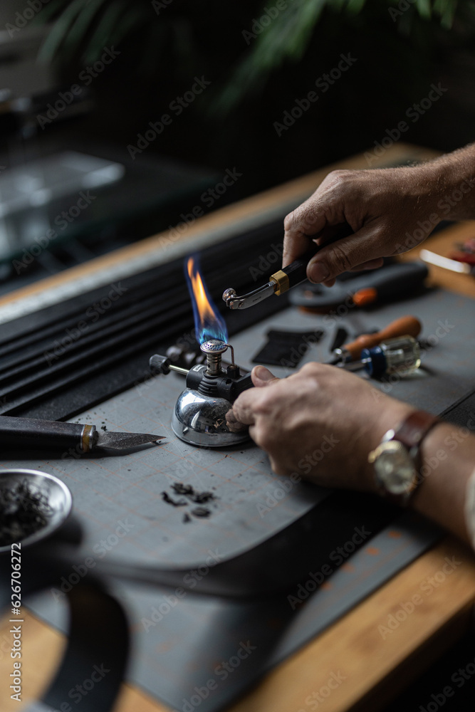 Man doing leatherwork, in a leather working workshop, making a black leather belt Man doing leatherwork, in a leather working workshop, making a black leather belt