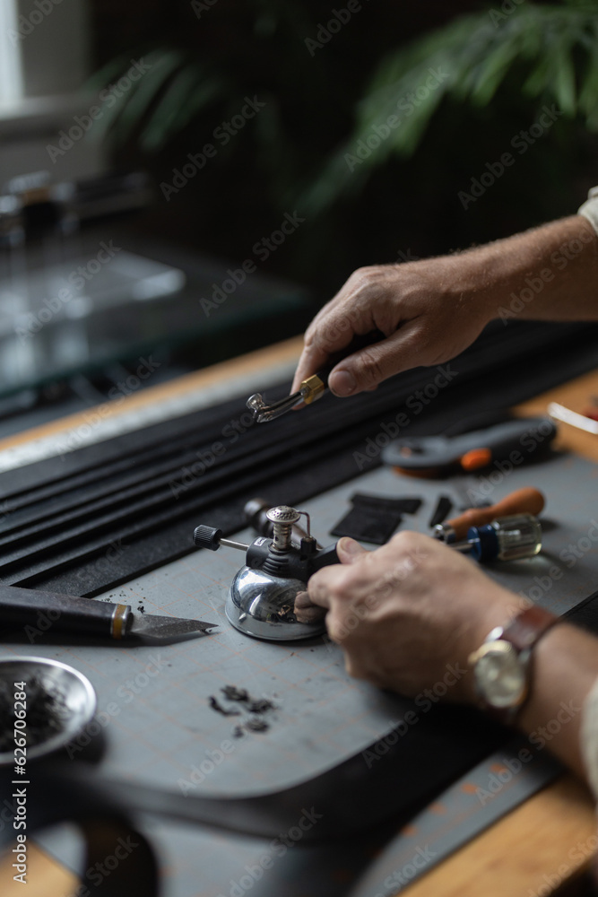 Man doing leatherwork, in a leather working workshop, making a black leather belt
