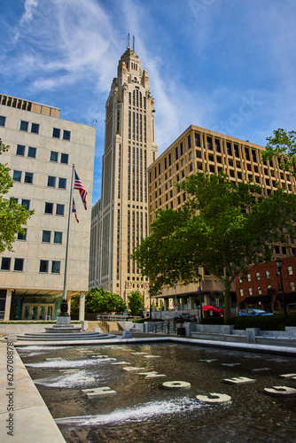 Stone words at bottom of fountain with American and Ohio flags and LeVeque Tower in background
