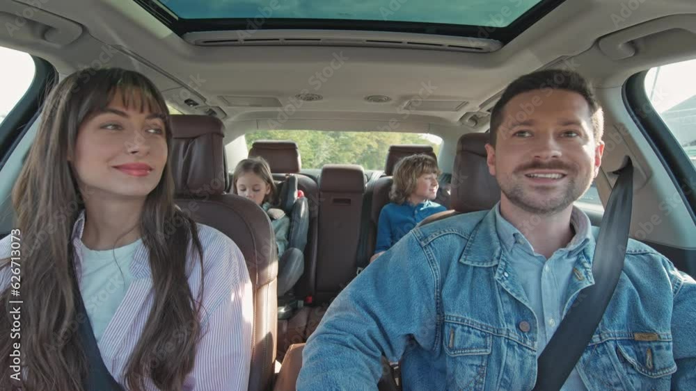 Mom and dad laughing and joking with their kids while traveling by car. Having so much fun during the road trip. Young parents driving their kids to the beach. Concept of happy parenthood. Mom and dad laughing and joking with their kids while traveling by car. Having so much fun during the road trip. Young parents driving their kids to the beach. Concept of happy parenthood.