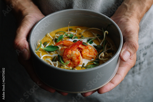 pumpkin soup with shrimps and stracciatella  in male hands

