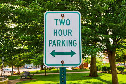 Close up of green Two Hour Parking sign in front of a park in summertime