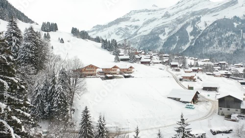 Drone flying away from distant cabins in snow covered rural landscape and revealing pine trees photo