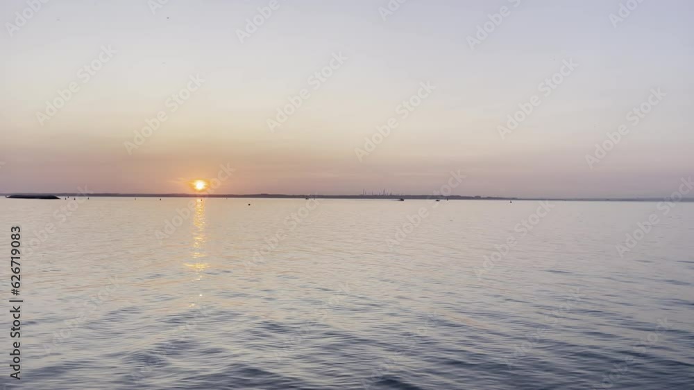 Landscape shot of the sun setting over a calm ocean, sun a bright orange colour Landscape shot of the sun setting over a calm ocean, sun a bright orange colour
