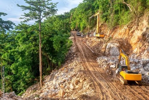 Heavy construction equipment at work building the foundation for a new road through a steep, forested area on Mindoro Island, Philippines.