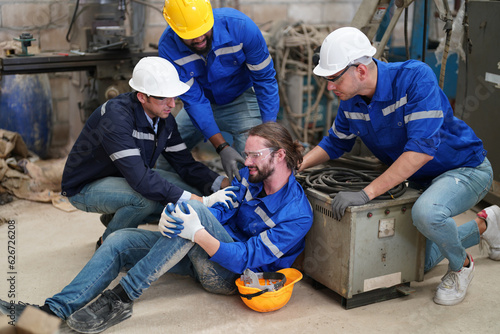 Fotografie Worker receiving industrial injury in factory and colleague helping him while  injured on leg