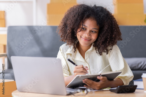 Startup SME small business entrepreneur of freelance African woman using a laptop with box Cheerful success African woman her hand lifts up online marketing packaging box and delivery SME idea concept