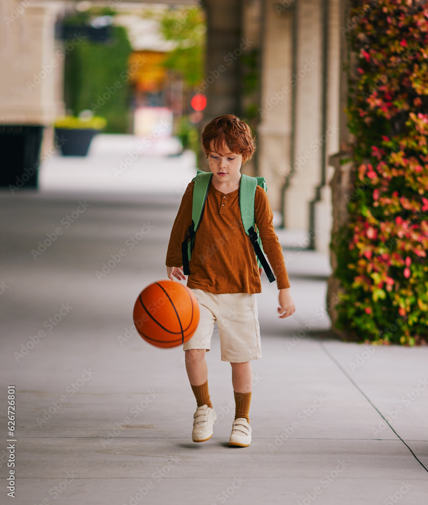 cute redhead school kid with basketball walking back from school