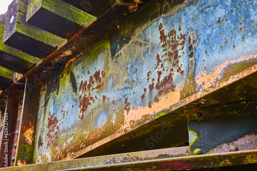 Blue and yellow rust corrosion on underside of railroad train bridge with wood beams from tracks