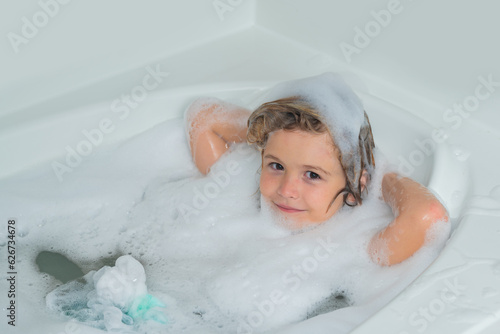 Bath tub with soap bubble. Funny boy with wet curly hair taking a bath in a kitchen sink with lots of foam.