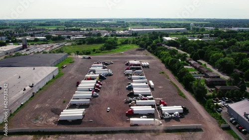 sideways aerial yard parking lot with semi trucks and trailers - reefers, dry van, flatbeds, stingers, bob tails. Truck Driver is backing up. Plainfield Illinois USA photo