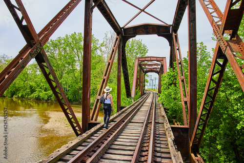 Woman walking across train tracks on railroad bridge over river in summer photo