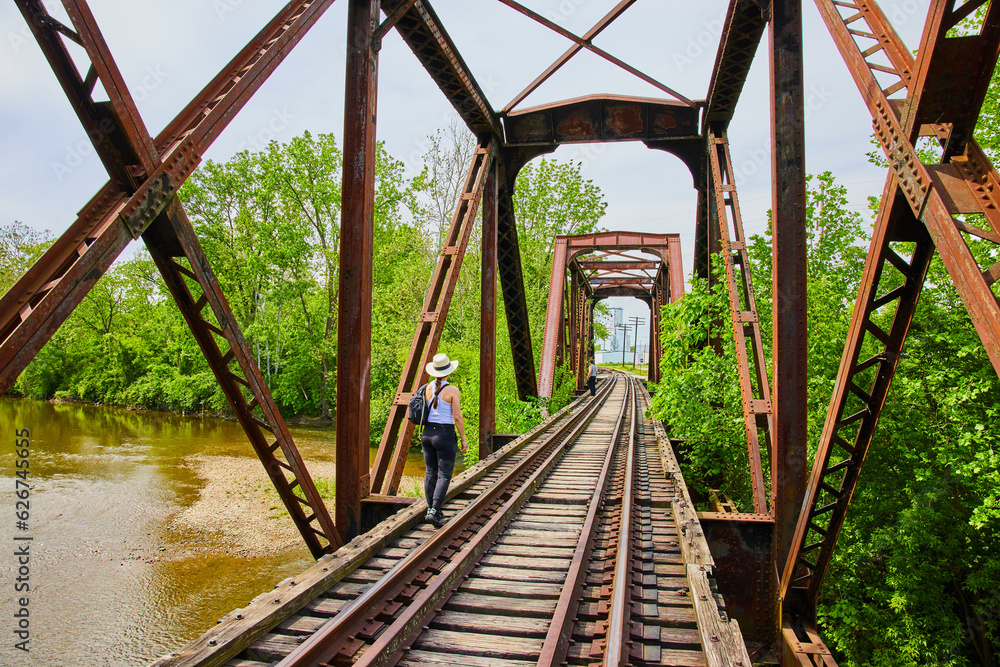 People walking on railroad tracks across bridge with river flowing underneath