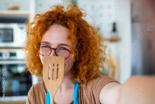 Obraz na plátne Young ginger woman,food blogger, snaps a selfie with a wooden spoon