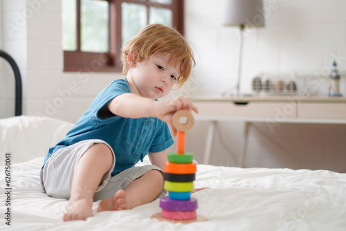 Kid play alone with a toy on bed at home. Little boy playing developing colorful blocks. Kindergarten education game. Learn and Play Concept.