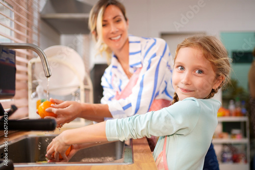 Happy cute daughter and mother washing fruit oranges together in a kitchen sink getting ready to cook orange juice for drink. Nutrition vitamin c, healthy food.