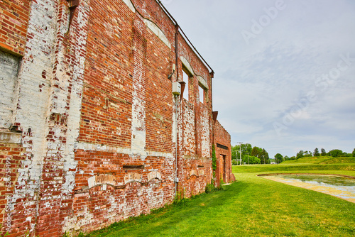 Partial wall of destroyed factory with red and white bricks with no roof and exposed to nature