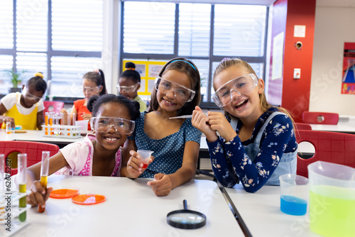 Portrait of happy diverse schoolgirls with chemistry items and liquids in elementary school class