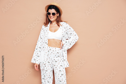 Young beautiful smiling female in trendy summer costume clothes. Carefree woman posing near beige wall in studio. Positive model having fun indoors. Cheerful and happy. In hat and sunglasses © halayalex
