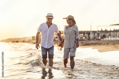 A middle-aged couple walking hand in hand on the beach at sunset