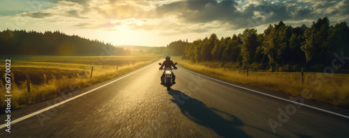 Driver riding motocycle on empty road in sunset light. Panorama photo.
