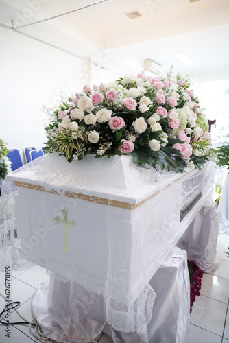 White coffin with a beautiful arrangement of pink flowers on the lid at a funeral ceremony and farewell