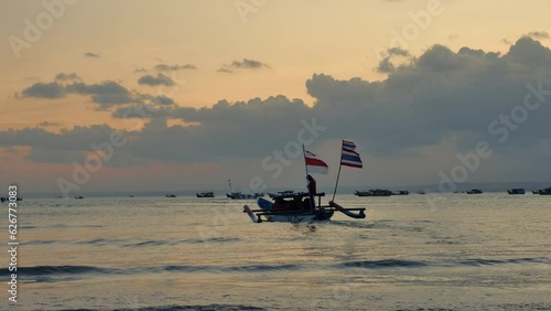 A man piloting a boat with a group of tourists at Pangandaran beach during sunset. Many fishing boats are seen sailing in the distance. Taken with handheld, slow motion, and telephoto lens. photo