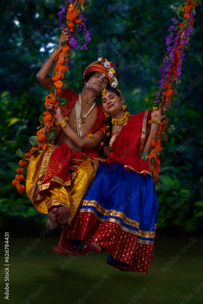 Young man and woman dressed up as Radha and Krishna and swinging together on a swing on the occasion of Janmashtami Young man and woman dressed up as Radha and Krishna and swinging together on a swing on the occasion of Janmashtami