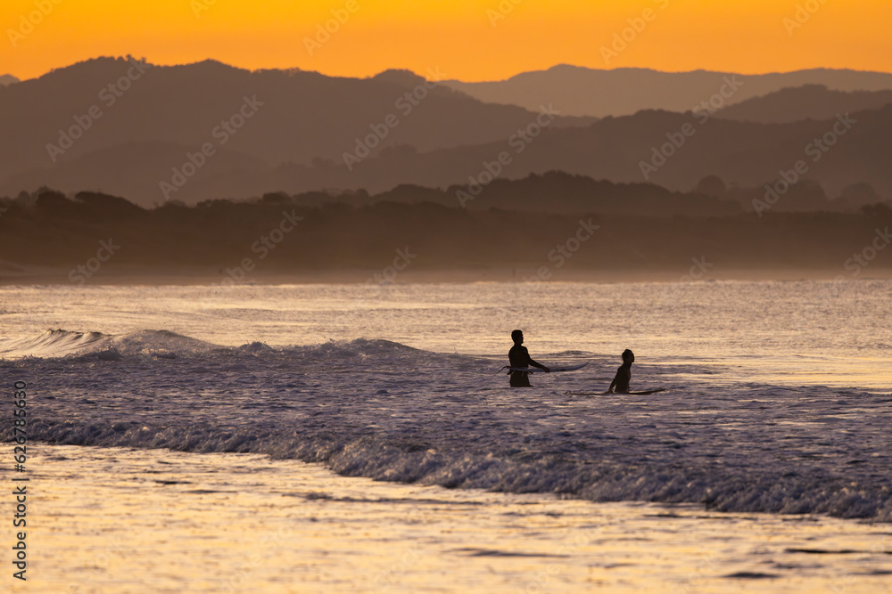Sunset view of surfers in silhouette along the Belongil Beach area in Byron Bay, New South Wales, Australia